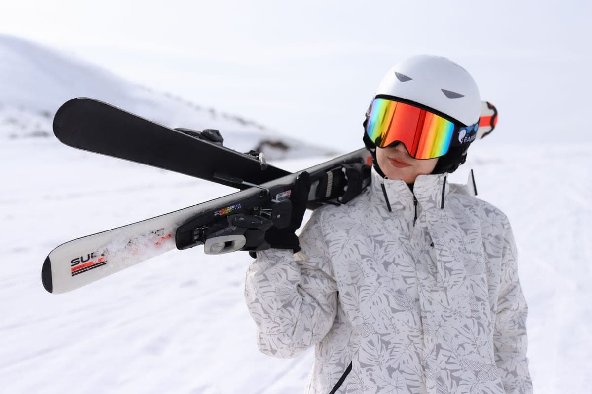 A person in ski gear carrying skis over one shoulder in a snowy mountain setting
