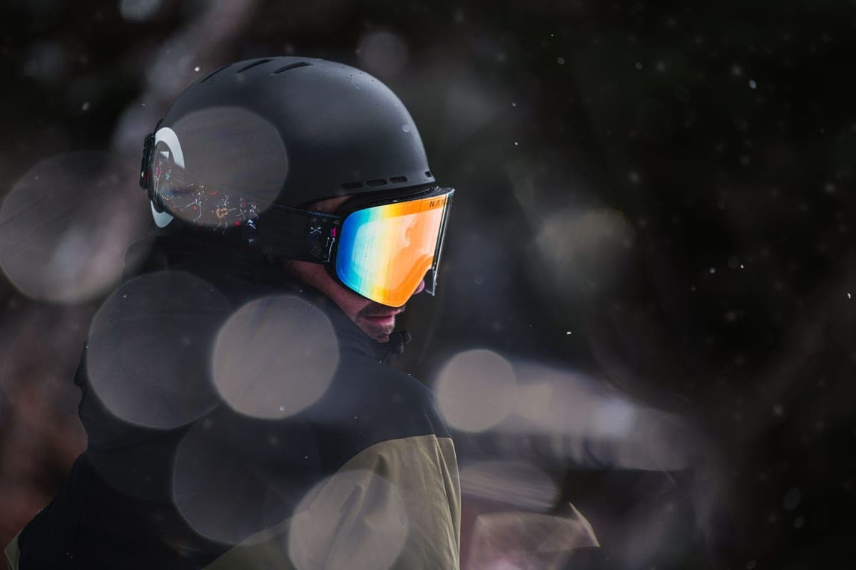 A snowboarder wearing a helmet and reflective goggles on a winter day